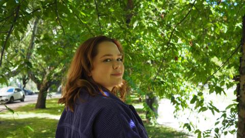 Nuori punatukkainen nainen seisoo vihreässä maisemassa ja hymyilee. 