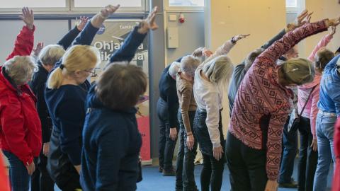 Senioreita osallistumassa liikuntatuokioon ja jumppaamassa seisten.