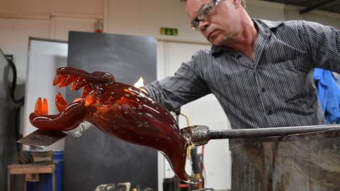 Lasinpuhaltaja Johannes Rantasalo työstämässä terävähampaista, punertavaa lasihirviötä.