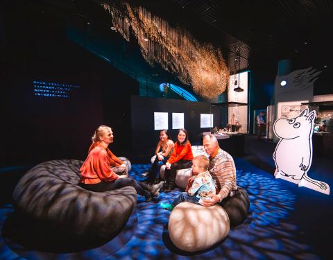 Adults and a child sitting on big pillows at Moomin museum.