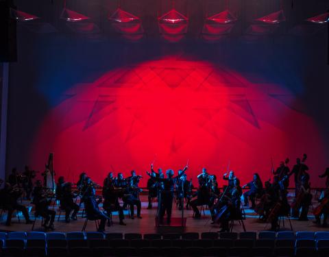 Tampere Filharmonia esiintymässä lavalla hämyssä, taustalla punainen valo.