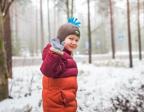 Lapsi vilkuttaa lumisessa metsässä.