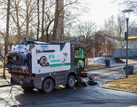 A brush tractor cleans the pavement in Kirjastonpuisto Park.