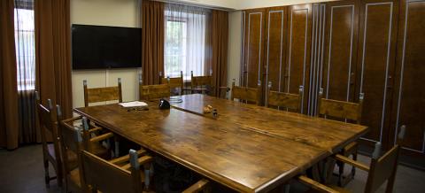 Neuvotteluhuoneen täyttää tummansävyiset puukalusteet. Keskellä huonetta on suuri pöytä ja sitä ympäröi tuoleja.