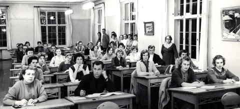 Henkilöt istuvat pulpeteissa luokkahuoneessa.