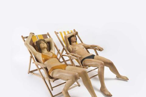 Veistos, jossa kaksi bikiniasuista naista istuu aurinkotuoleissa. 