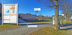 The Sarvis building is depicted from Hatanpäänkatu. On the left, you can see a large gray sign indicating the area. On the right, there is a bus stop. The image is marked with a pedestrian route that runs to the right of the sign. Above the building, there is the text “Entrance, Staircase F.” The entrance is located approximately in the middle of the long Sarvis building. 