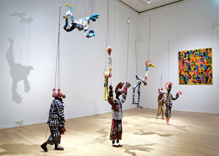 Yaya Coulibaly: Marionettinukkeja, 2006, taustalla Tingatinga –tyyliä edustava teos Sayuki: Paholaisia, 2005.
