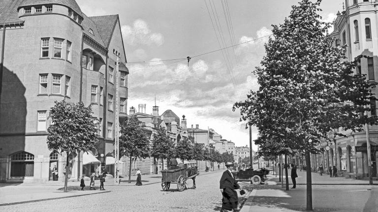 Raukean kesäinen alkuillan hetki Hämeenkadun ja Kuninkaankadun risteyksessä vuonna 1913. Kaupunkilaiset liikkuvat jalan, hevosella tai taksilla. Vasemmalla on Blomin talo ja oikealla Pulla-Helinin talo. 