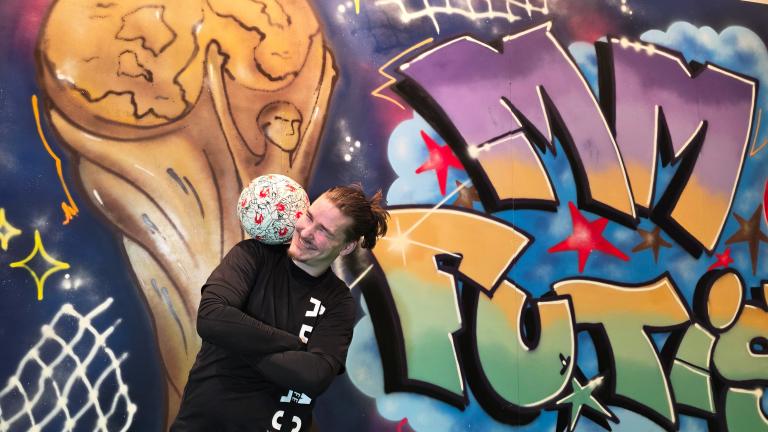 Mies temppuilee jalkapallon kanssa. Taustalla värikäs graffiti maalaus, jossa teksti MM Futis.