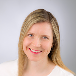 Henkilökuvassa hymyilevä vaaleahiuksinen nainen katsoo kameraan.