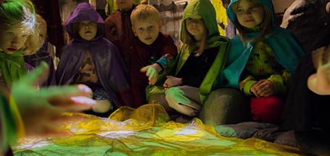 The children sit around a green play pond dressed as forest dwellers.