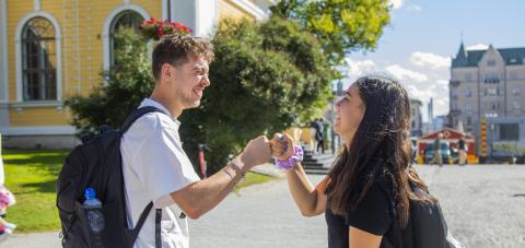 Two young adults greet each other with a &quot;fist bump&quot; on Central Square in the sun.