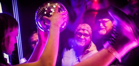 Diskopalloa käsissään pitävä hahmo esiintyy ikkunan takana kadulla seisovalle yleisölle. 