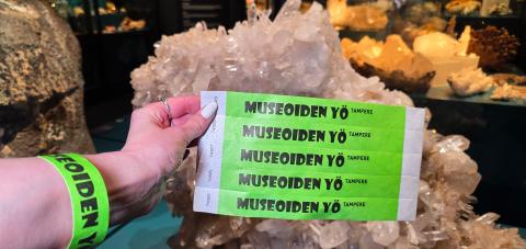 Vihreitä Museoiden yö -rannekkeita kuvan etualalla ja henkilön ranteessa. Taustalla kiviä näyttelytilassa.