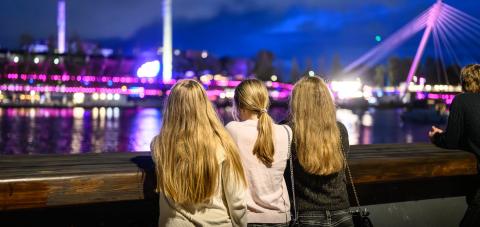 Kolme nuorta nojaa kävelysiltaan selät kameraan päin iltaisessa Tampereessa.