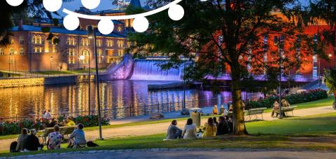 Koskipuisto Park illuminated at night, with people sitting on the grass area along the rapids.