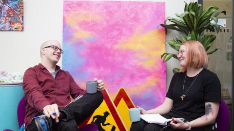 Kaksi ihmistä istuu kahvikupit kädessä vastakkain. 