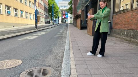 Vihreätakkinen nainen kuvaa mobiililaitteella ritiläkaivon kantta kadulla.