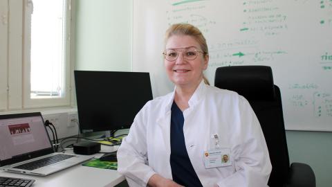 Anna Maria Heikkinen työpöytänsä ääressä valkoinen hammaslääkärin takki päällään.