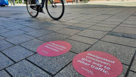 Punaiset pyöreät merkinnät Hämeenkadun jalkakäytävän pinnassa kertovat ylityspaikasta.