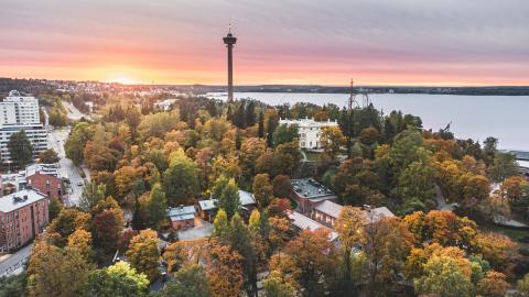 Ilmakuva Tampereelta auringonlaskun aikaan syksyllä. Kuvassa näkyy Näsinneula, Näsijärveä sekä taloja ja syksyn kellastuttamia lehtipuita. 
