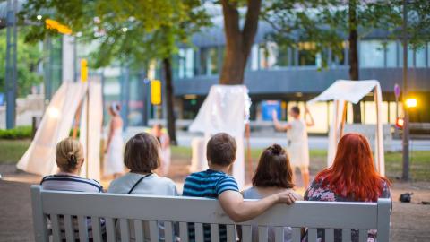 Ihmisiä katselee puistonpenkillä esitystä Tampereen Teatterikesässä