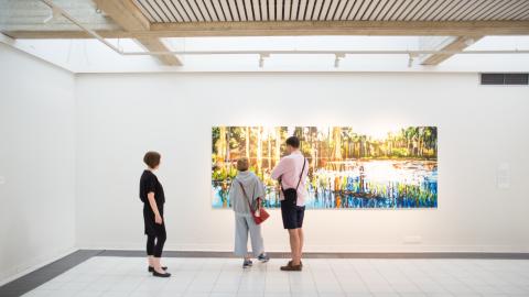 Kolme henkilöä katsoo taidemaalausta Sara Hildénin taidemuseossa.