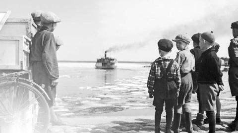Järvellä höyrylaiva, lapsia seisoo rannalla katsomassa laivaa. Mustavalkoinen kuva.