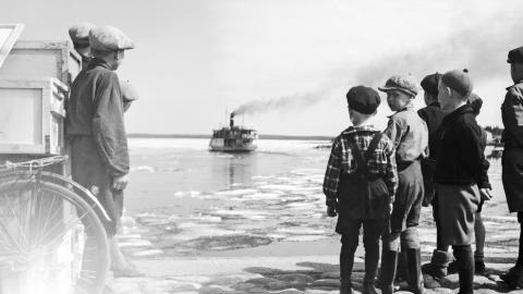 Mustavalkoisessa valokuvassa pienet pojat katselevat poispäin kulkevaa höyrylaivaa Näsijärven rannalla. 