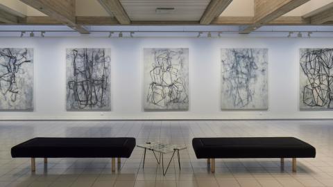 Näkymä Jukka Mäkelän näyttelystä, jossa seinällä on ripustettu viisi harmaasävyistä maalausta, joissa on hiilellä piirrettyjä kuvioita.