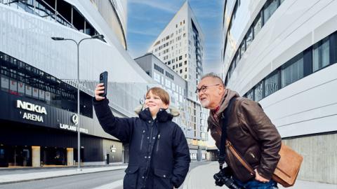 Kuvassa poika ja mies katsomassa ottamassa kännykällä valokuvaa Nokia Arenan edessä.