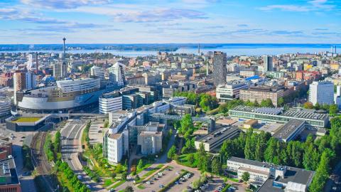 Aerial view of Tampere city centre in summer, the sun is shining, the sky is blue, the trees are green and there are tall buildings in the background.