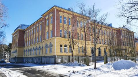 Pyynikintie 2 -kiinteistö, joka on vanha, kelta-punainen iso koulurakennus, talvisessa näkymässä.