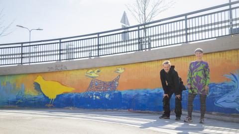 Kuvataiteilija Sebastian Schultz ja kuvataideopettaja Riikka Ajanki seisovat nuorten maalaaman ympäristöaiheisen muraalin edessä