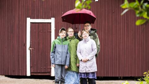 Lantelankallion perhe seisoo punaisen varaston edessä punaisen sateenvarjon alla.