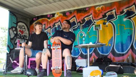 Kaksi nuoriso-ohjaajaa istuu graffiteilla koristetussa kontissa ja juttelee keskenään hymyillen.