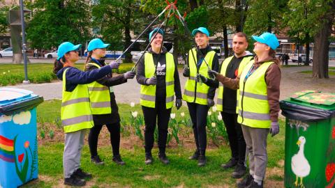 Kuusi vastuullisuusagenttia seisoo keltaisissa työliiveissä ja turkooseissa lippalakeissa Posteljooninpuistossa Tampereella roskapihtien kanssa.