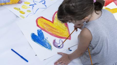 Puistoruokailutapahtumassa oleva tyttö maalaa vesiväreillä sydämiä.