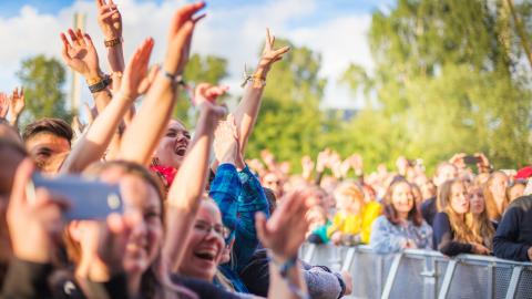 Kesällä iloisia ihmisiä kädet ilmassa Tammerfestin esityksen aikana.