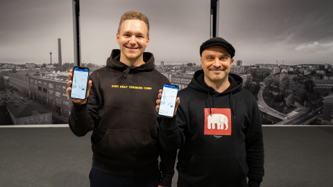 Kaksi miestä hupparit päällä seisoo ja hymyilee kameralle. Molemmilla on kädessä älypuhelin, jossa Tampereen Pulssi -palvelu on päällä.