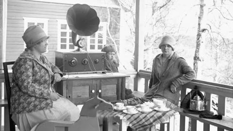 Kaksi naista ja lapsi kuuntelevat radiota terassilla.