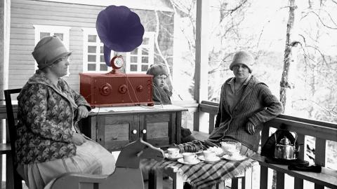 Kaksi naista istuu ulkona vanhanaikaisen radion ympärillä. Kuva on mustavalkoinen.