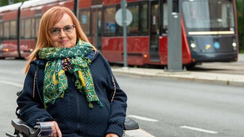 Rita Järvinen sitting in a wheelchair on the street, with a tram in the background.
