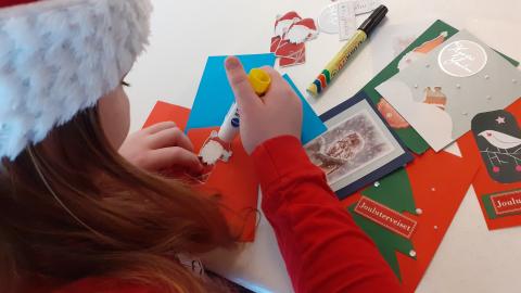 Tonttulakkinen nuori askartelee iloisen värisiä joulukortteja Joulupostia ikäihmisille -kampanjaa varten.