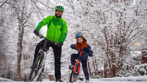 Isä ja poika pyörien kanssa talvella puiden alla.