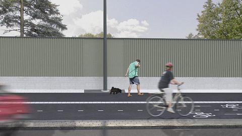 Paneloitua meluseinää kadun varressa, pyöräilijä kulkee pyörätiellä ja koiran ulkoiluttaja  jalkakäytävällä.