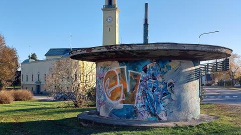 Värikkäiden graffitien peittämä lankarullakioski etualalla ja kioskin takana on Viinikan kirkko torneineen. 