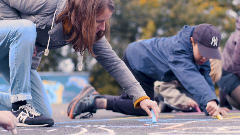 Aikuinen ja lapsi piirtävät yhdessä liiduilla asfalttiin.