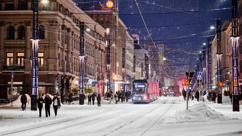 People and a tram in the snow on Hämeenkatu in the evening.